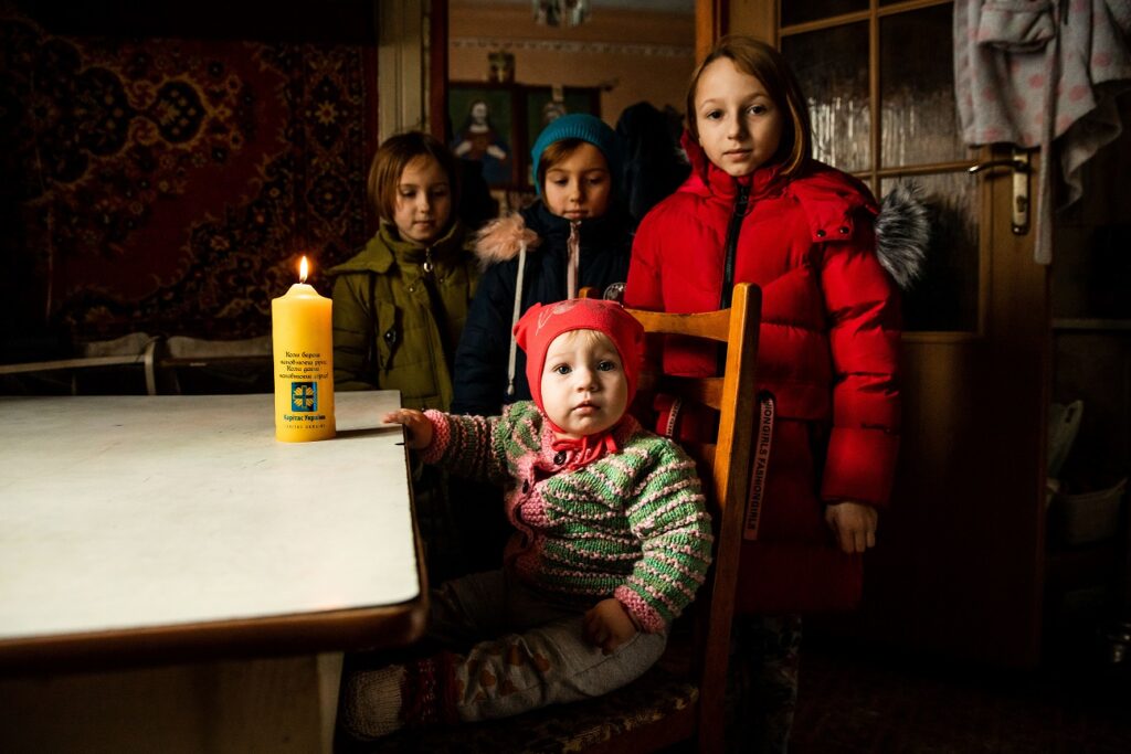 Родина з дітьми вдома за столом із жовтою різдвяною свічкою Карітасу