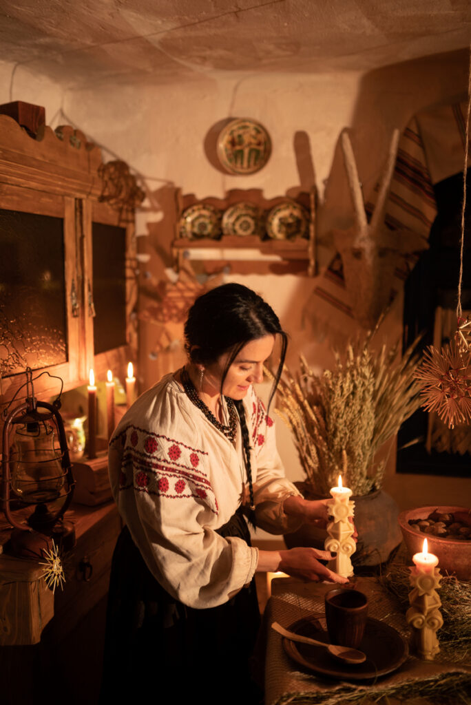 Жінка у вишиванці запалює фігурні різдвяні свічки Карітас у хаті з дідухом