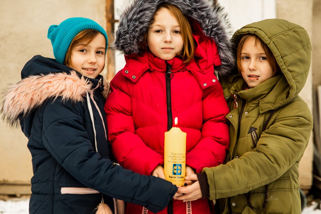 Діти взимку тримають різдвяну свічку Карітасу